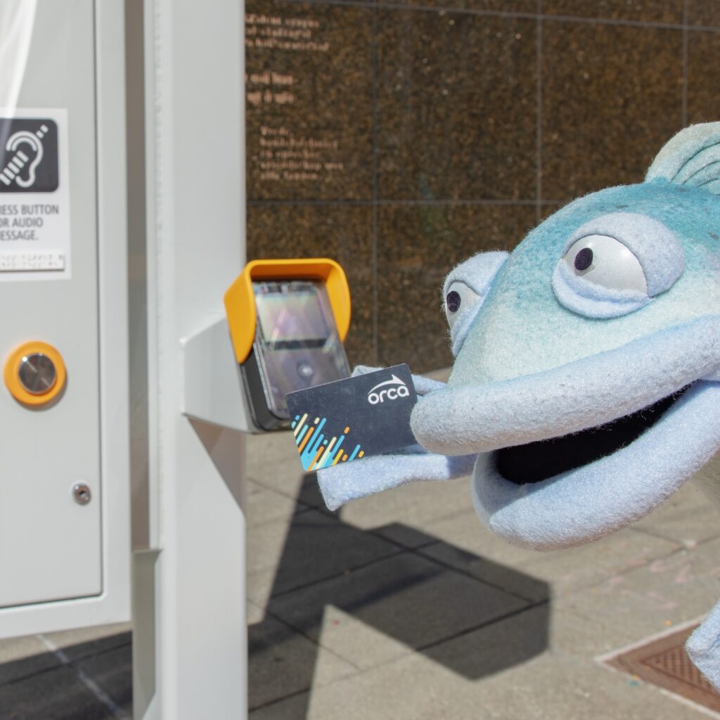 Sal the Salmon taps an ORCA card on the reader to pay bus fare at a RapidRide stop.
