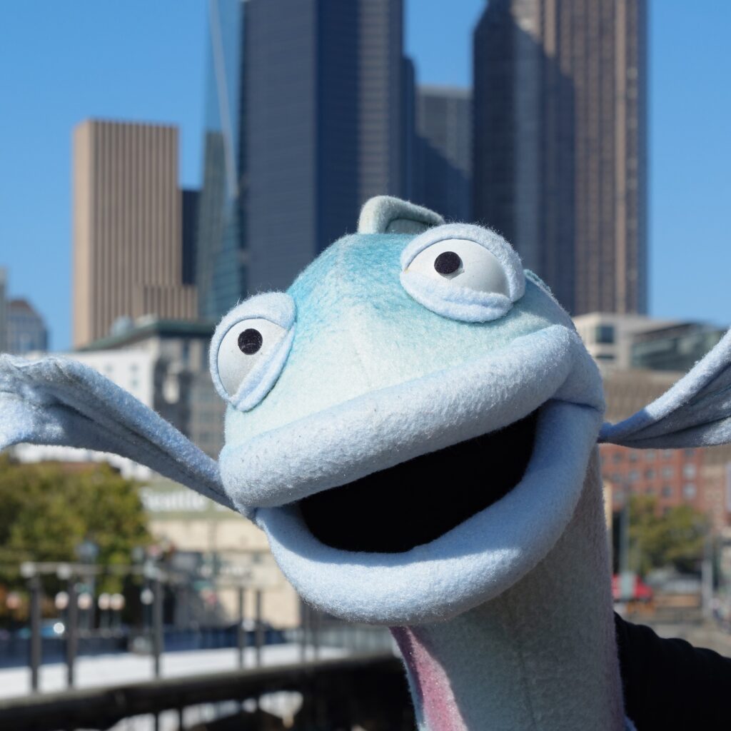 Sal the Salmon waves with Downtown Seattle in the background.