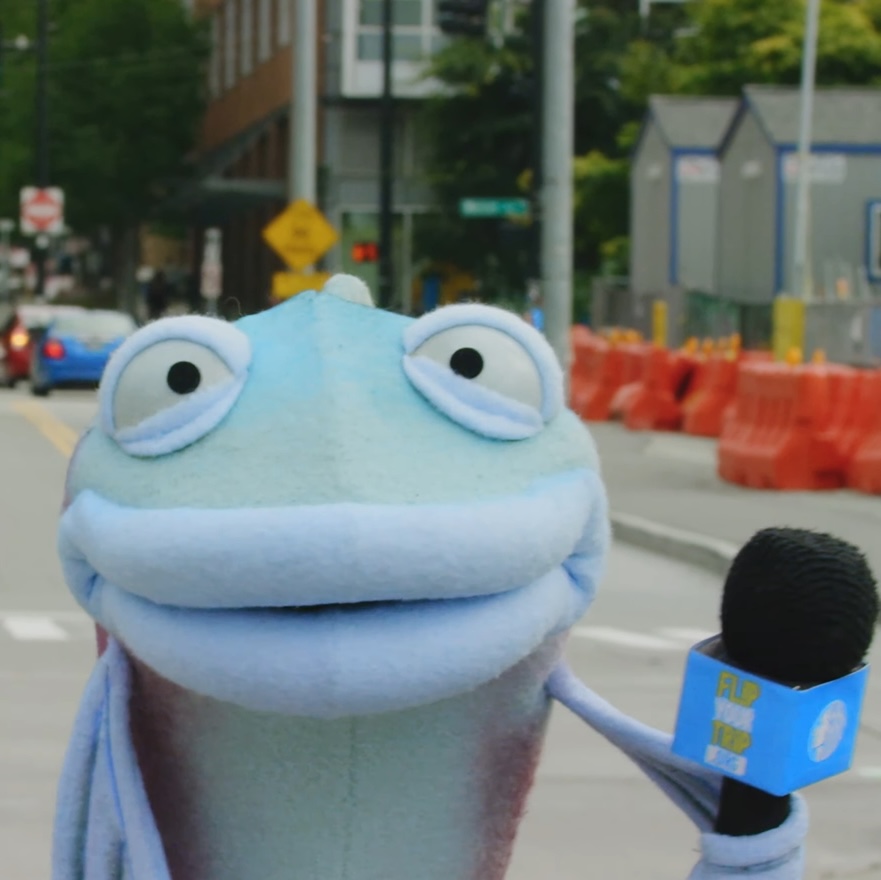 Sal stands with a microphone in the middle of a street while a street car turns in the background