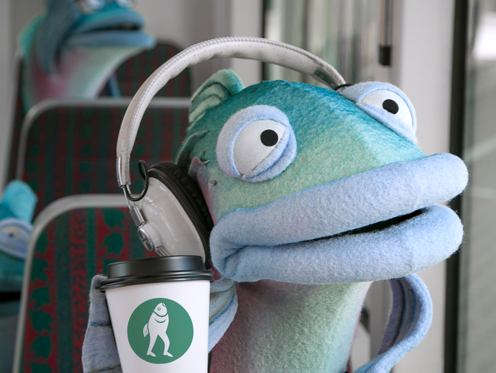Sal the Salmon sits in the Seattle Streetcar looking outside the window with a coffee and headphones.